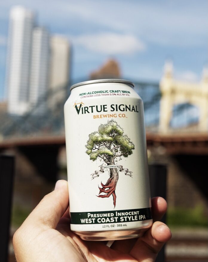 A person holds a white can of Virtue Signal beer in front of a bridge in Pittsburgh.
