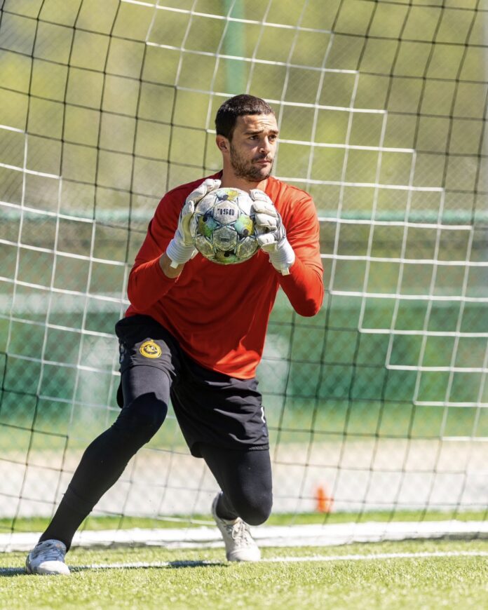 A soccer player holds a soccer ball in front of a net.
