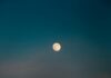 Your May 2026 Horoscope for the Full Moon in Sagittarius A full moon in a blue sky with orange-ish red clouds.