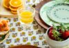 Stylish Melamine, Enamelware, and Paper Plates for Summer Picnics A stack of green paper plates on a pattern tablecloth with a glass of orange juice above it.