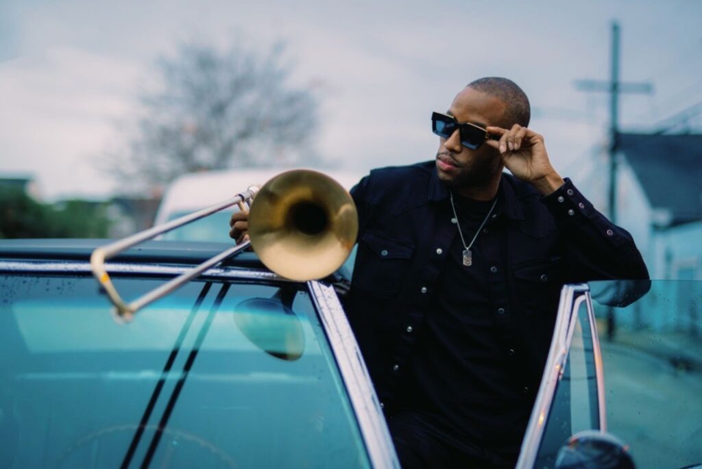A man with a trombone getting out of a car with sunglasses on.
