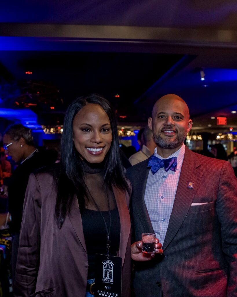 A man in a red suit and bowtie and a woman in a dark red blazer with drinks.