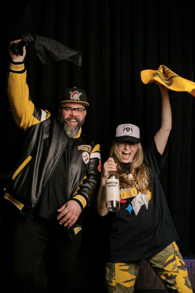 Two bartenders in Pittsburgh clothing holding Terrible Towels and a bottle of vodka.