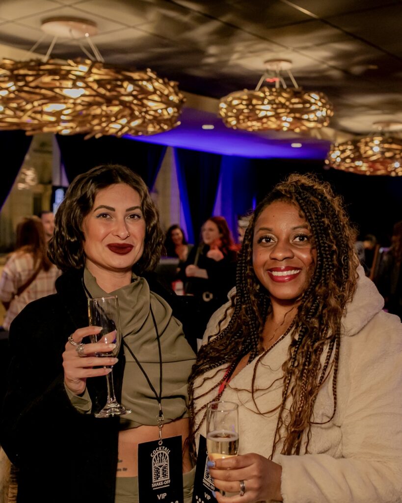 Two women smile holding cocktail glasses.