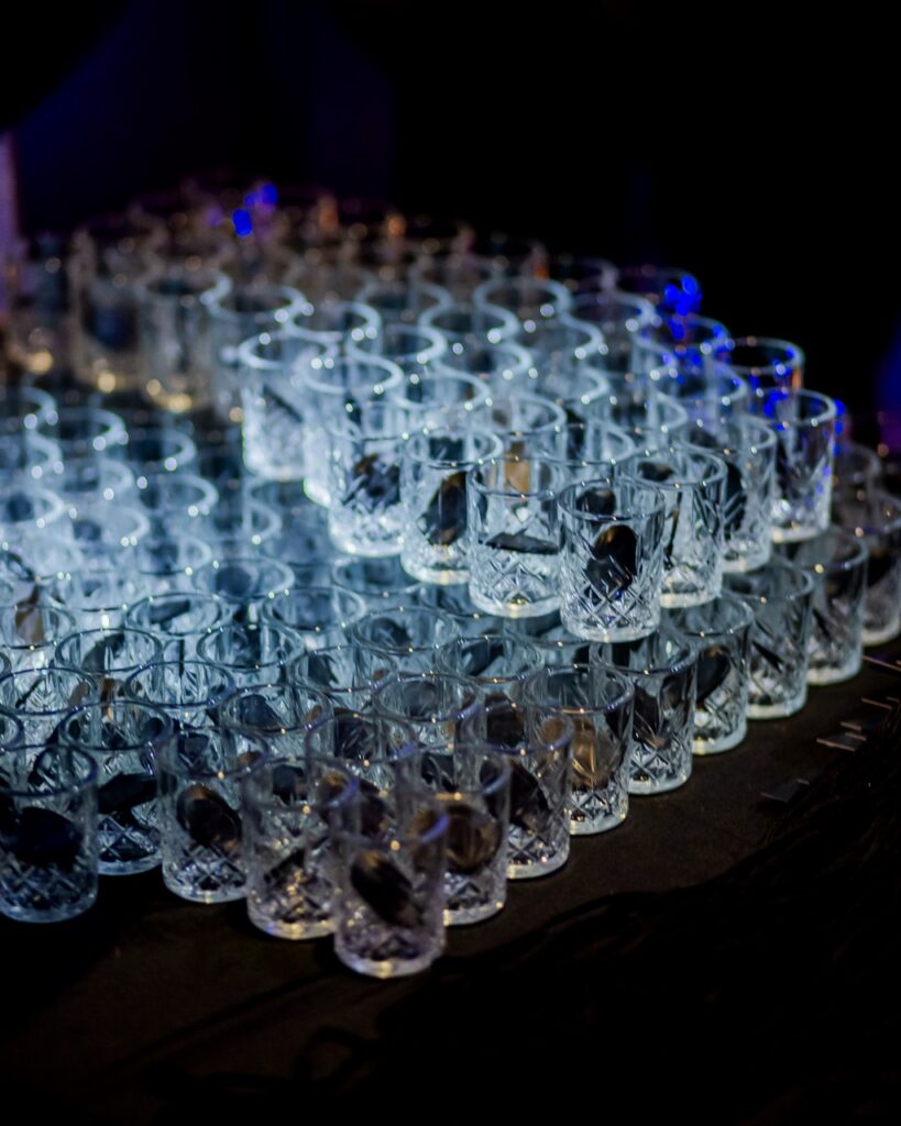 A bunch of small sampling glasses on a table with a light over top of them.