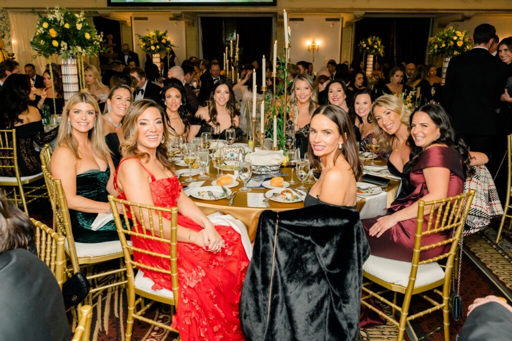 A group of women sit at a gold table with large candles in the center and gold chairs.