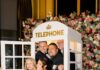 412 Gives Back Gala 2026 A group of men and women pose in a white telephone booth with flowers behind it.