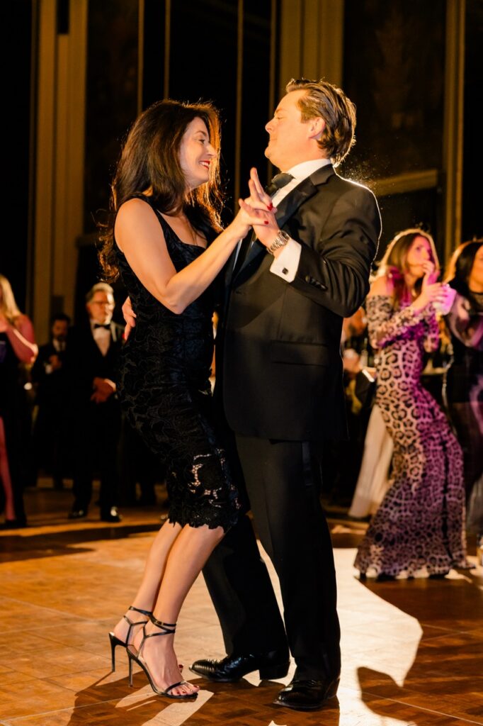 A couple in black evening wear dance together on the dance floor.