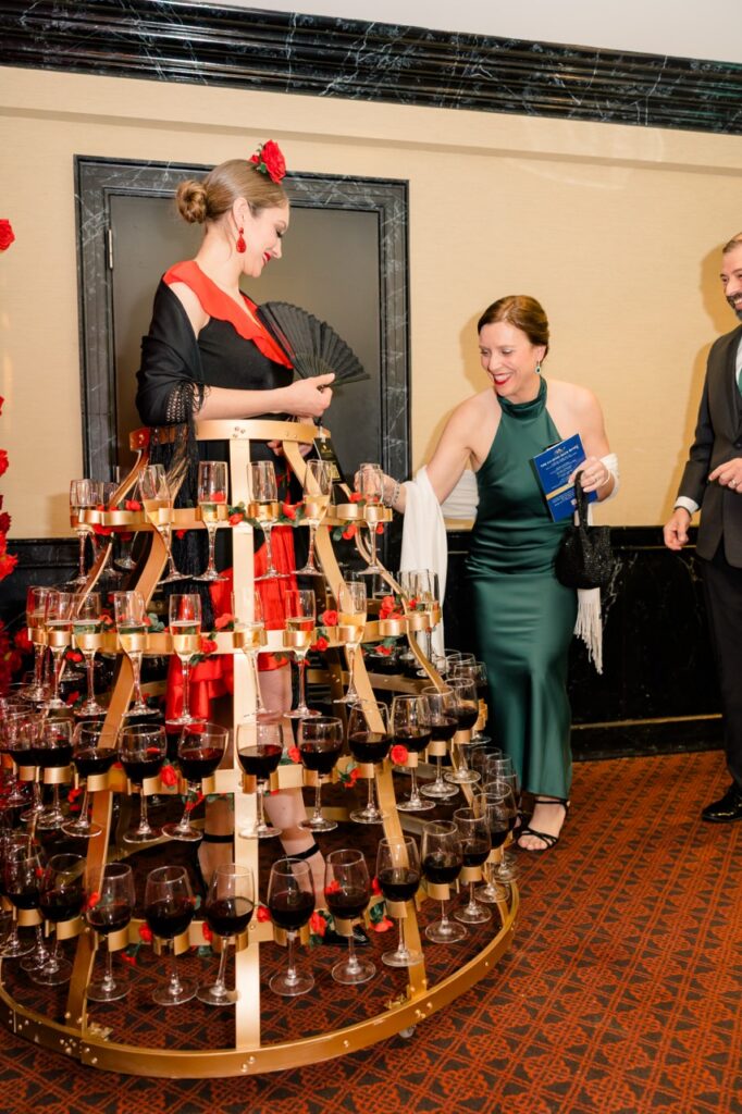 A woman takes a wine glass from another woman's large skirt.
