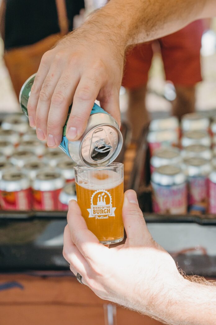 A person pours a can of beer into a beers of the burgh festival sampling glass.