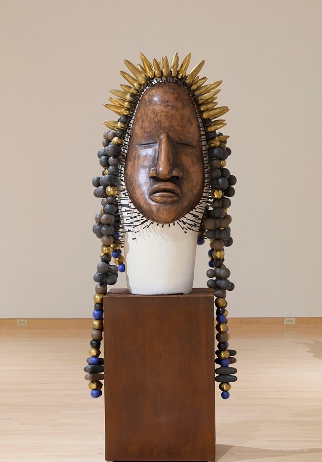A bronze statue head with a pointy crown and bulbs for hair.