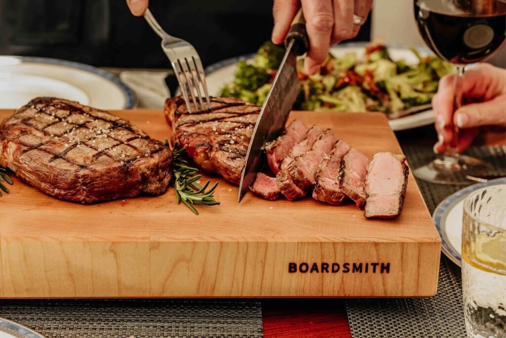 A person cuts up steak on a wood thick cutting board.