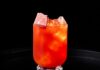 Carnegie’s Lunch: A PB&J Cocktail A PB&J cocktail in red and orange tones sits in a glass with ice on a black tray.