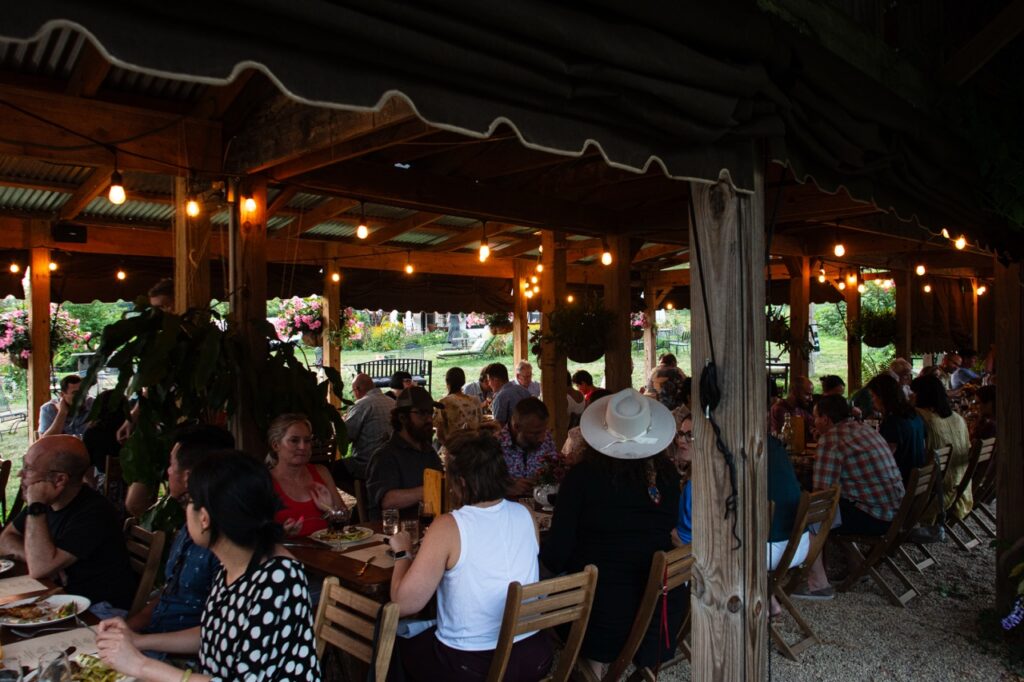 People eat at Churchview farms inside a fancy tent with lights above them and sitting at sturdy tables.
