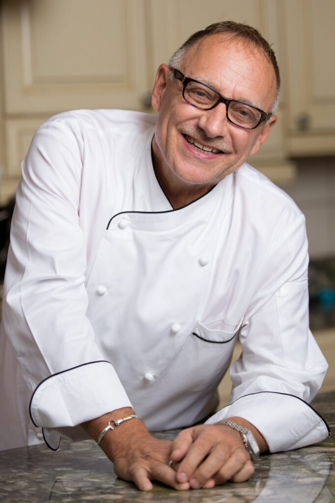 Chef Bob Sendall in a white chefs jacket and with black glasses on.