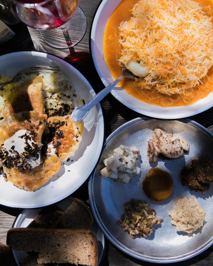 Three plates of vegan food with pierogies, small samples on another, and a bowl of orange soup with cheese on top.