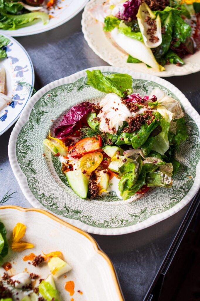 A salad sits on a plate with a green pattern along the edge. It's full of greens, purple leaves, and fruit.