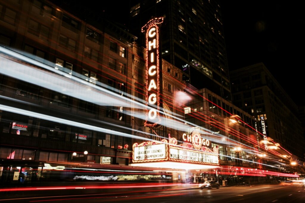 Cars zoom past the outside of a Chicago theater all lit up at night.