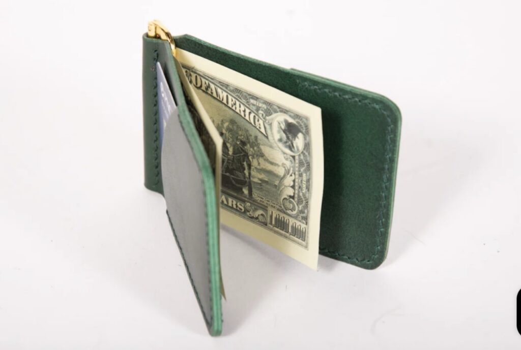 A green leather wallet open with money inside.