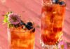 Earl Gray and Blueberry Punch Two tall glasses with Earl Gray and Blueberry Punch with blueberries on top and a flower garnish.