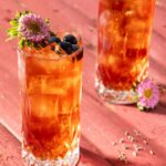 Two tall glasses with Earl Gray and Blueberry Punch with blueberries on top and a flower garnish.