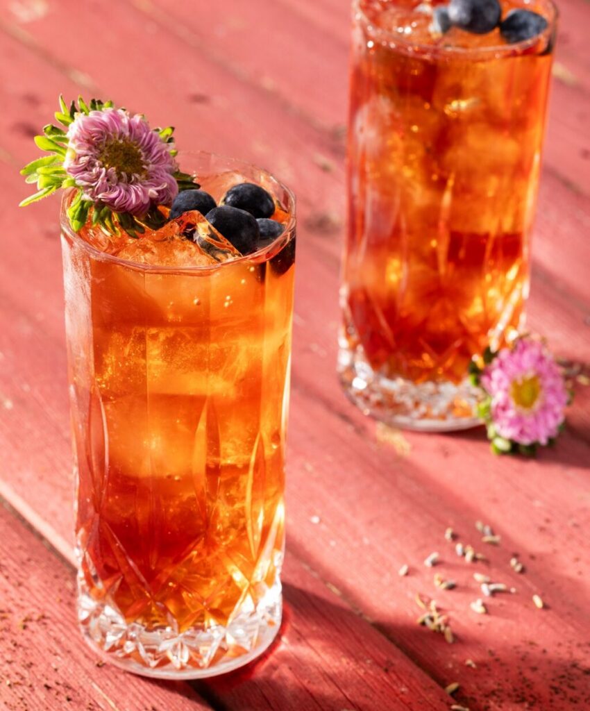 Two tall glasses with Earl Gray and Blueberry Punch with blueberries on top and a flower garnish.