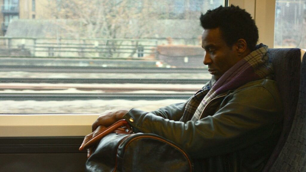 A man on a train looks down at his duffle bag in the window seat.