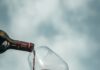 How to Navigate the Wine Selection at Fine Wine & Good Spirits Wine pours from a bottle to a glass help up against a blue sky.