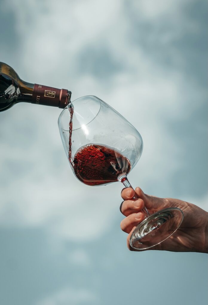 How to Navigate the Wine Selection at Fine Wine & Good Spirits Wine pours from a bottle to a glass help up against a blue sky.