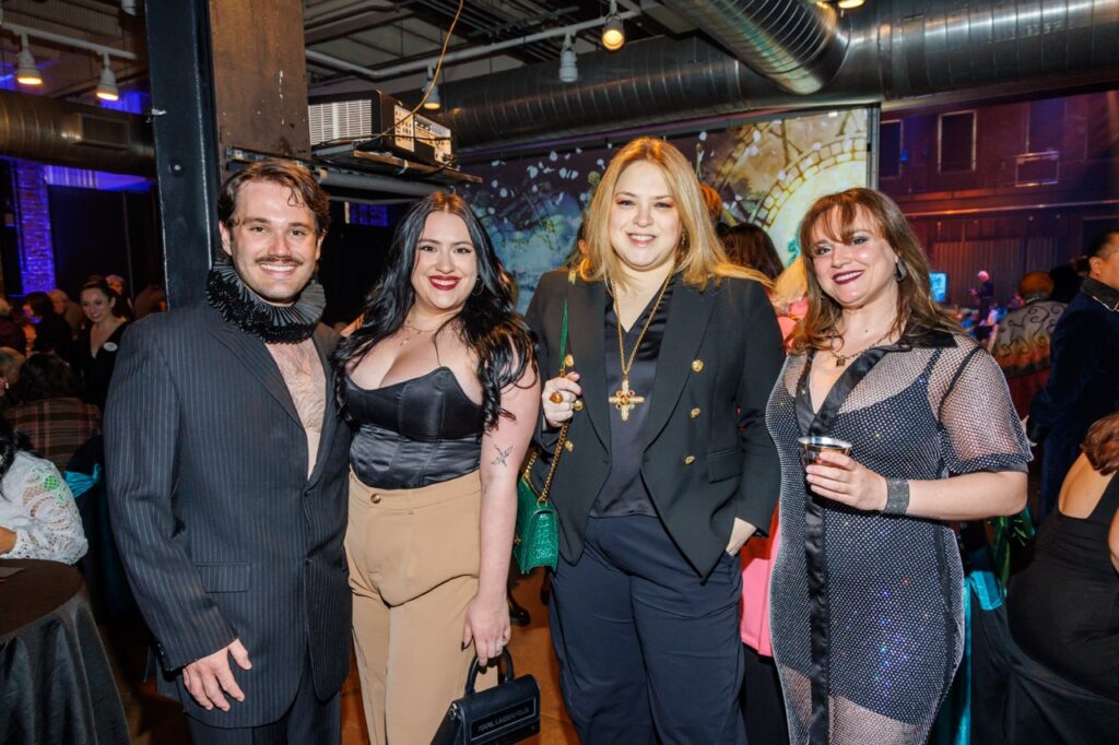 Three women and a man smile together in black and neutral outfits.