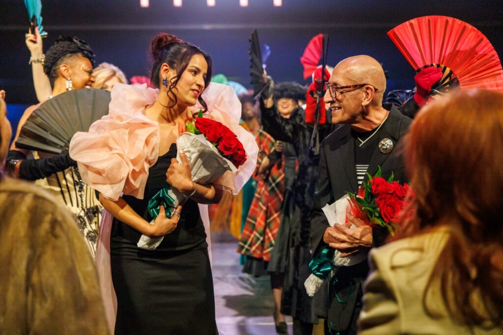 A woman with red roses looks over at a man with glasses also holding red roses.