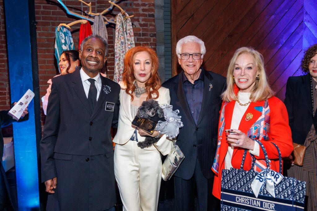 Two women and two men stand together as a woman with red hair holds a small black poodle dog.