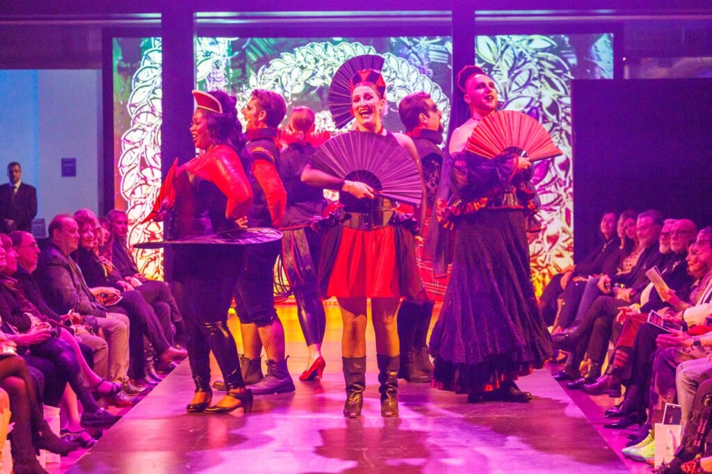 A group of Opera members in traditional skirts with hand fans in front of them.