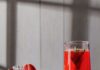 Juneteenth Red Punch (Berry Peach Lemonade) Three glasses of red punch beside a large pitcher of the punch with mint leaves inside and strawberries on the rim.