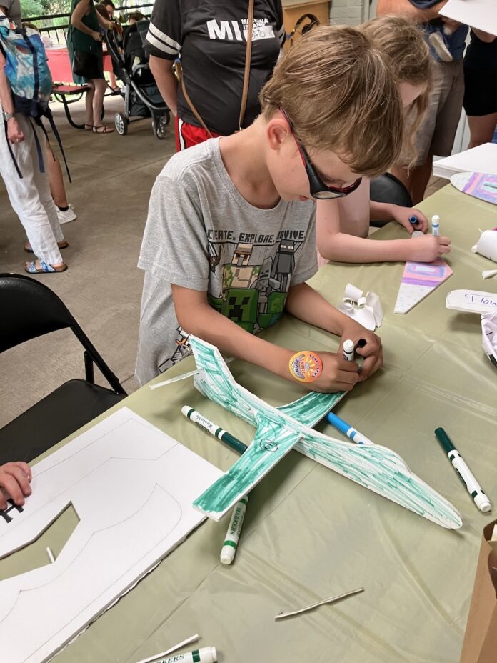 A kid colors a paper airplane green at the Carnegie Library.