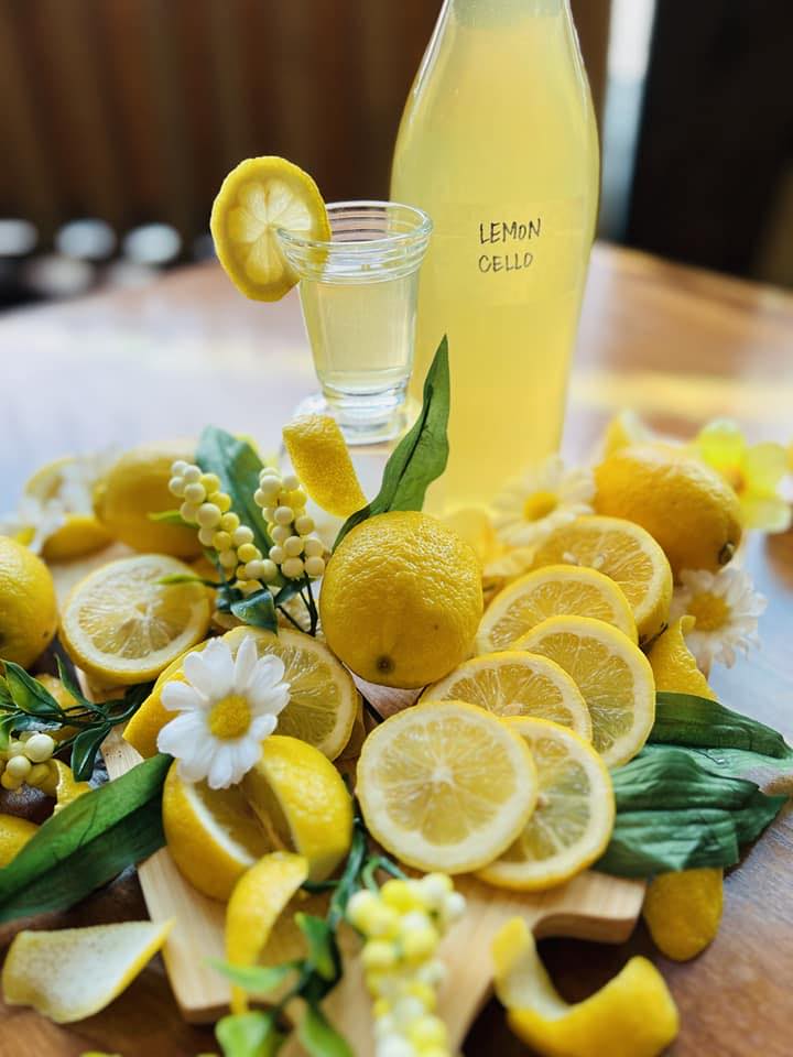 A bottle of Limoncello beside a table full of lemons and white flowers.