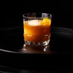 A Barley Tea Old Fashioned in a short cocktail glass with an orange peel garnish.