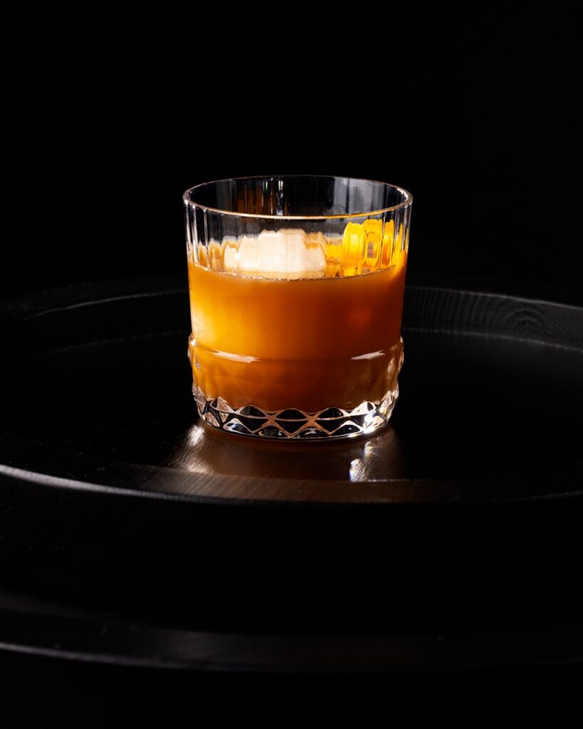 A Barley Tea Old Fashioned in a short cocktail glass with an orange peel garnish.