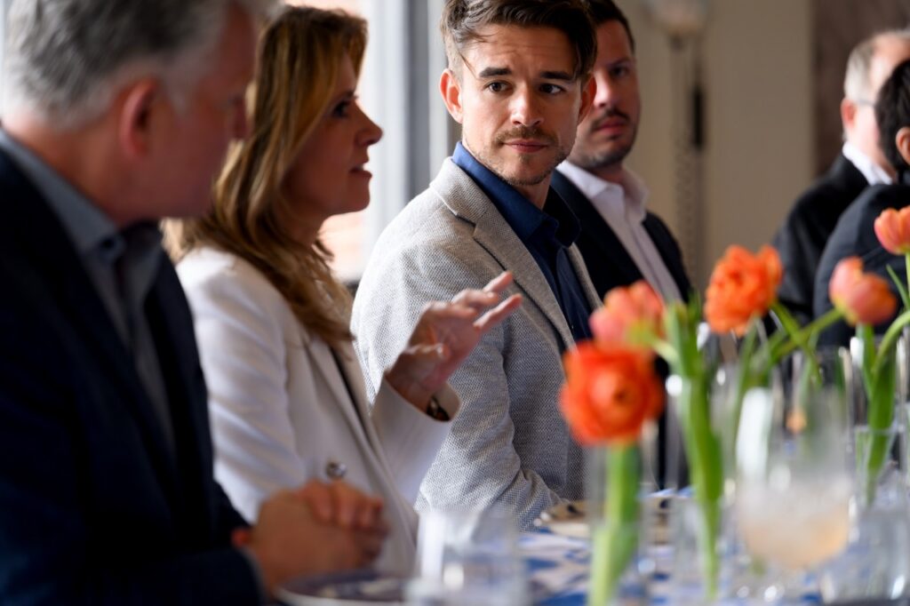 A man in a suit jacket watches a woman with blonde hair speak.