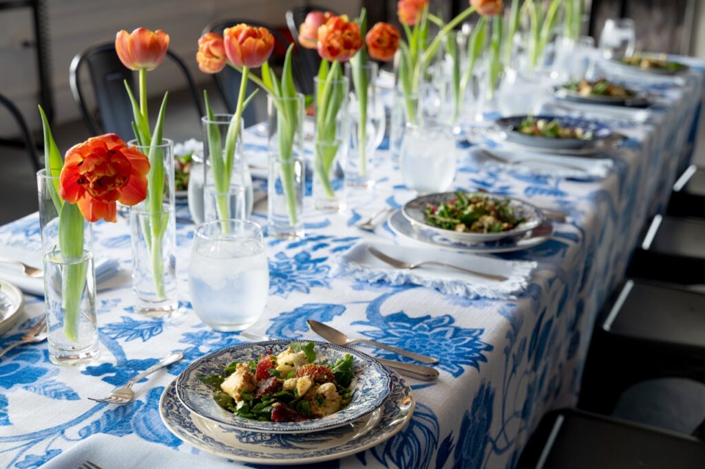A blue and white table cloth holds plates and orange flowers.