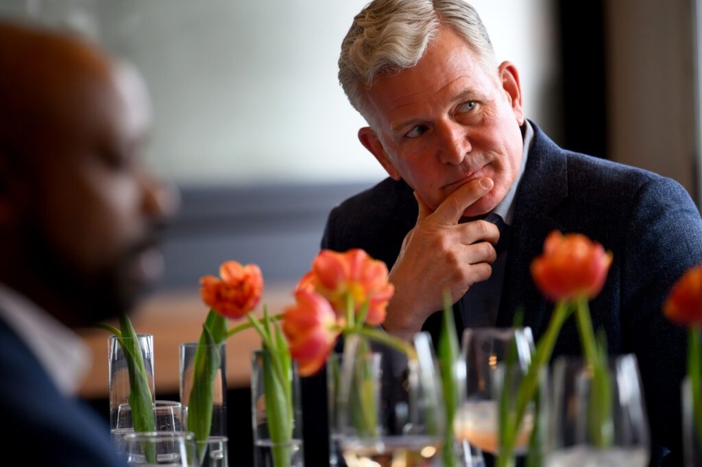 Keith Recker leans forward with intrigue at the table, his hand on his chin.