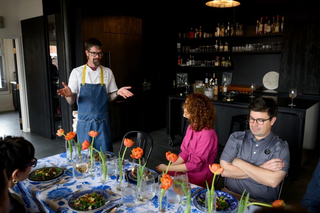 Chef Kevin in a blue apron talking to the table.