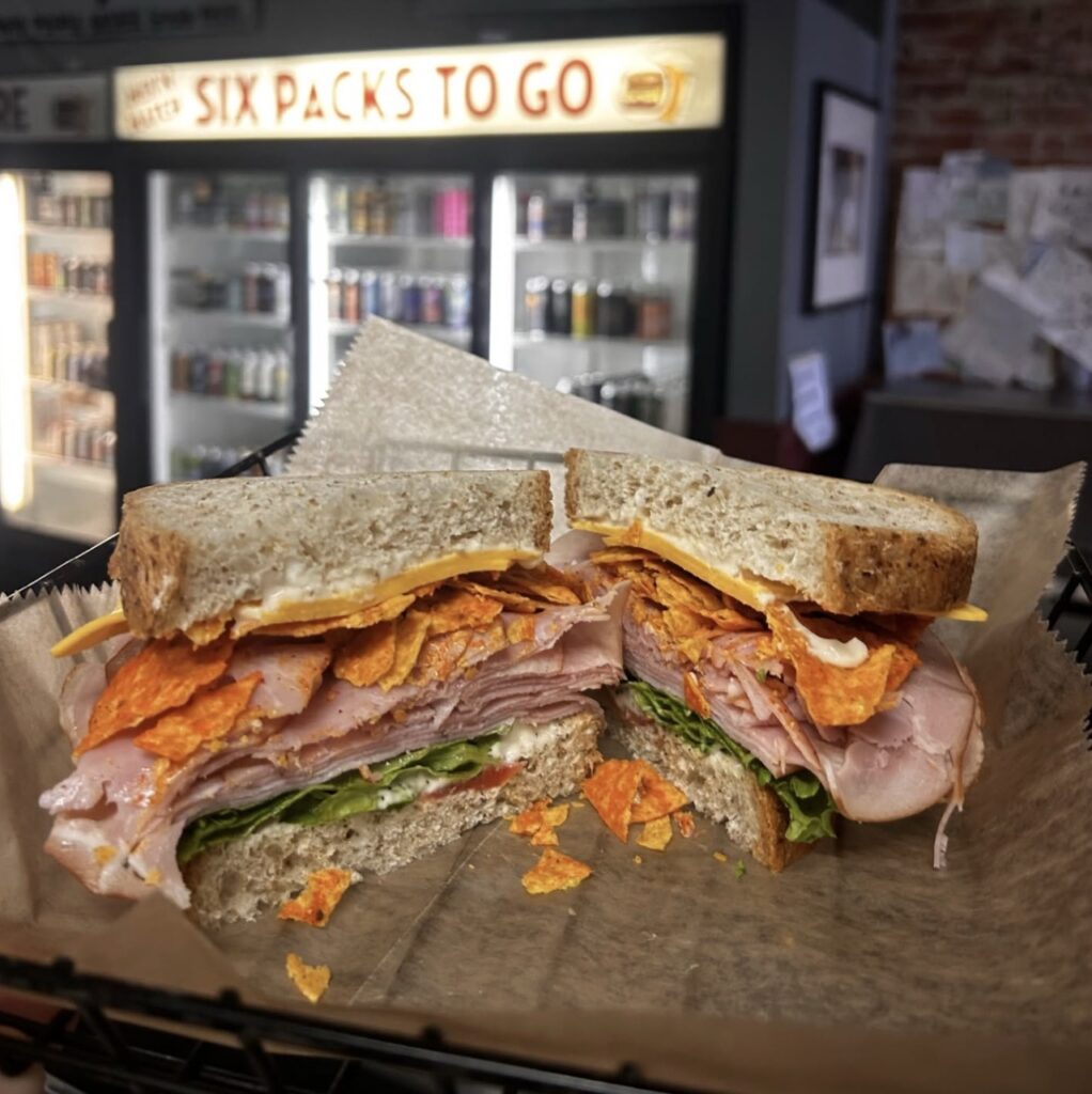 A sandwich on wheat bread with meat, veggies, and chips.