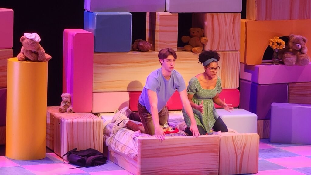 Two people on a block bed surrounded by blocks on a stage.