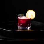 A short cocktail glass with a spicy blueberry drink inside and a lemon wheel as a garnish.