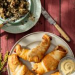 Pigs in a blanket beside a side of mustard and a bowl of sauerkraut.