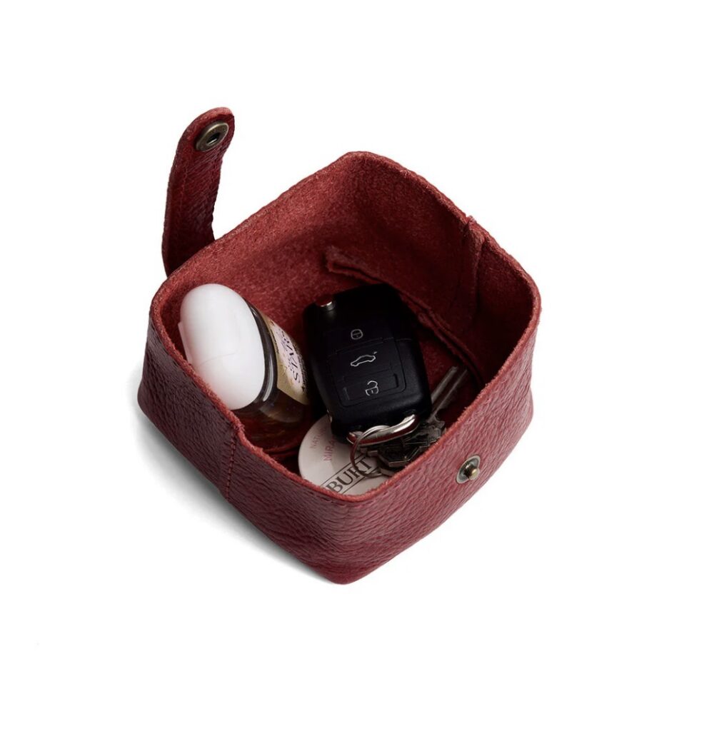 A small red leather square pouch holds keys and hand sanitizer.