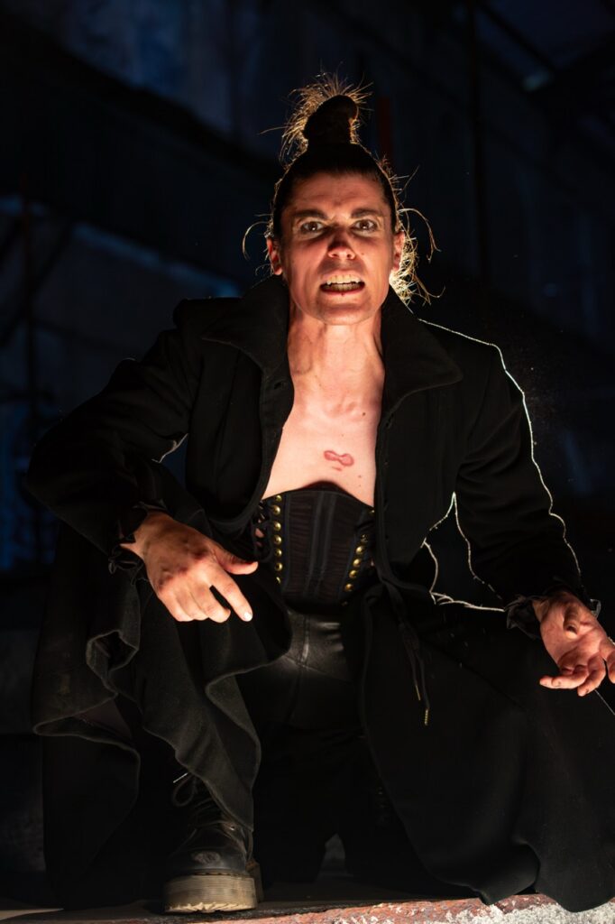 A person in a corset and black jacket crouched down on stage.