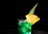Caribbean Dream Alcoholic Punch A green alcoholic punch in a short cocktail glass with ice, a pineapple slice garnish, and a pineapple leaf garnish.