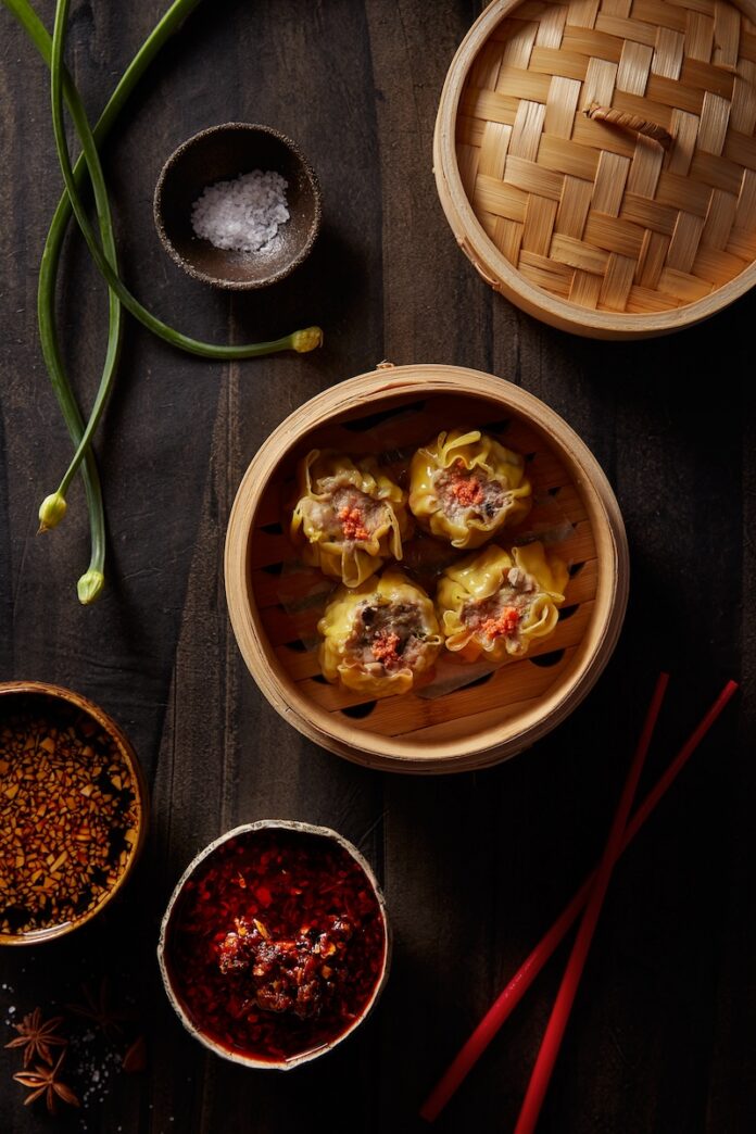 A steamer of four dim sum with a pair of red chop sticks sitting underneath it.